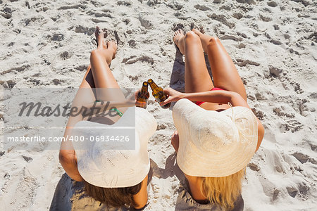 Sexy blonde and brunette on the beach wearing straw hat clinking their glass bottle