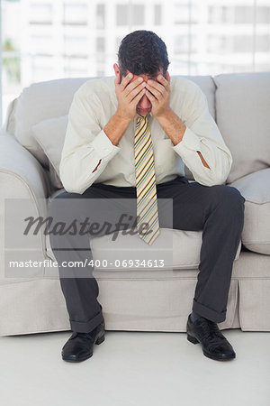 Troubled businessman sitting on sofa in bright office