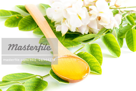 Honey in spoon with acacia flower and leaves on white background