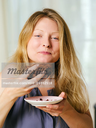 Photo of a beautiful blond woman in her early thirties with log blond hair eating a large piece of brownie or cake.