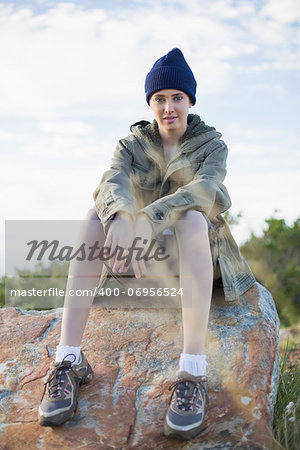 Woman wearing cap sitting on stone looking at camera