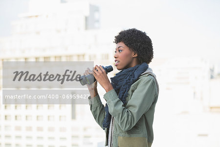 Curious casual model holding binoculars outdoors on a sunny day