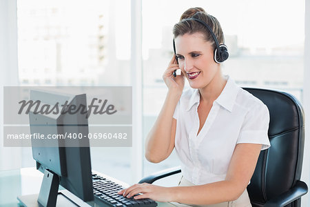 Cheerful call centre agent working on computer while having a call in bright office