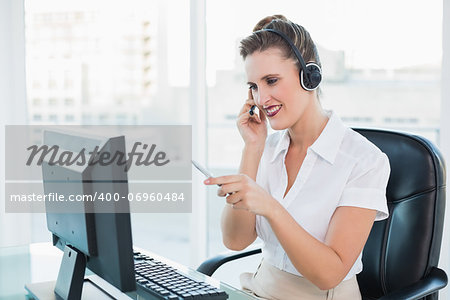 Smiling call centre agent pointing at something on computer screen in bright office