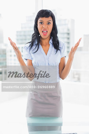 Irritated businesswoman looking at camera and raising her arms in office