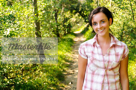 A smiling young Caucasian girl wearing mountain clothes on a hiking path in the wood