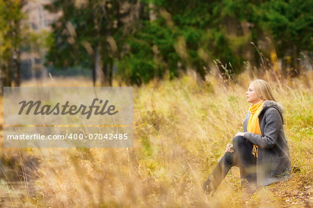 beautiful blond girl sitting on rivershore in autumn forest