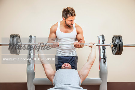 A handsome young muscular sports man doing weight lifting and gets help from his friend
