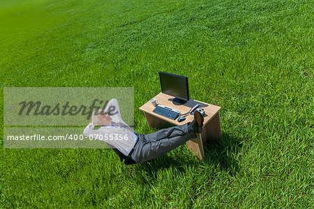 Business aerial high angle concept shot showing an older male man or businessman relaxing feet up at a desk with a computer in a green field