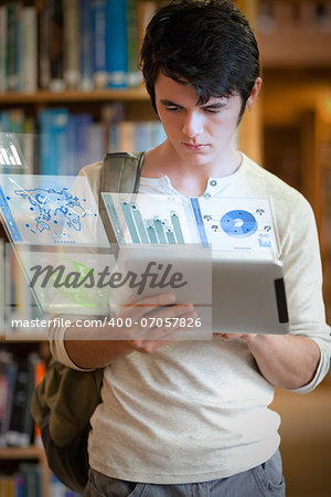 Serious handsome student working on his futuristic tablet pc in university library