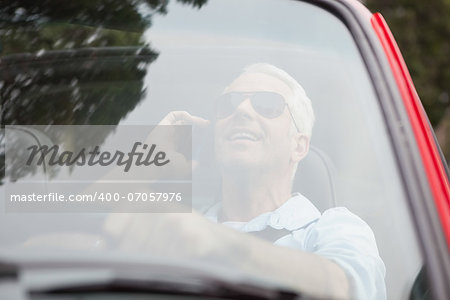 Smiling handsome man in red convertible having phone call while driving