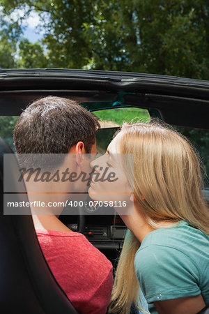 Attractive blonde kissing her boyfriend while having a ride in cabriolet on a sunny day