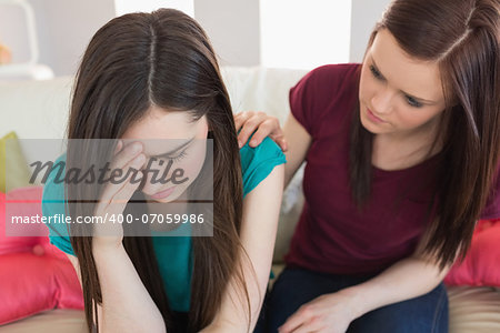 Girl comforting her crying friend on the couch at home in living room