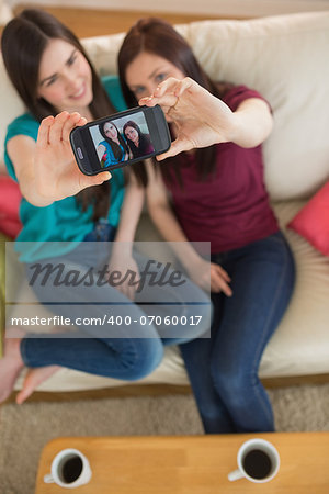 Two friends on the couch taking a selfie with smartphone at home in the living room