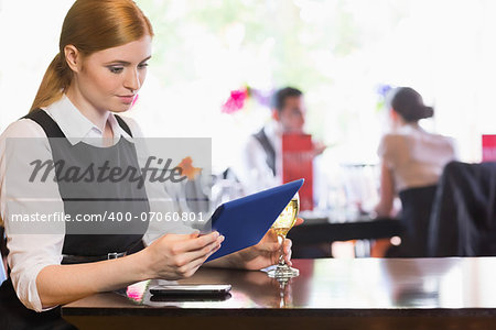 Businesswoman looking at tablet screen while holding wine glass in a restaurant