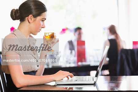 Attractive businesswoman holding wine glass while working on laptop in a restaurant