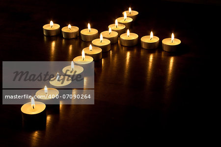 Lit tea lights in the shape of a cross on a polished wooden surface.