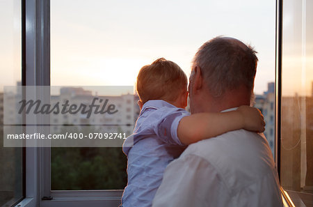 Grandfather holds and embracing grandson on the balcony during sunset