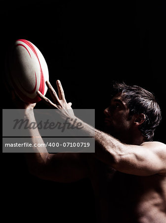 one caucasian sexy topless man portrait hugging a rugby ball on studio black background