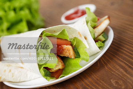 wheat tortilla with chicken and vegetables on plate on wooden table