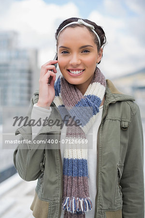 Stylish woman talking on phone while looking at camera outside