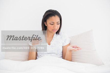 Worried young dark haired model taking medication in bright bedroom