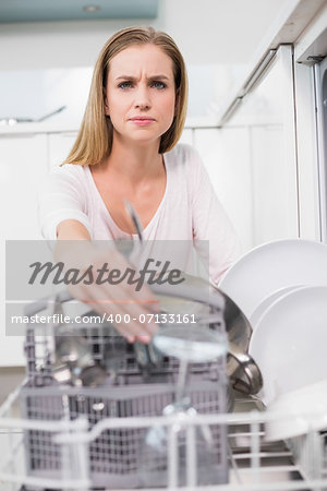 Frowning gorgeous model kneeling behind dish washer in bright kitchen