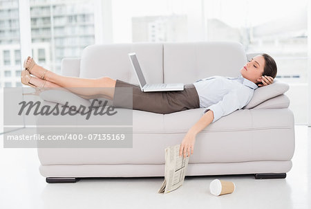 Side view of a young woman with laptop sleeping on sofa at home