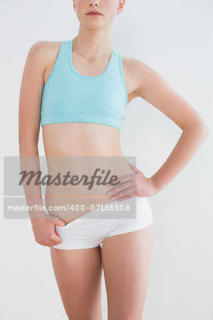 Mid section of a toned young woman standing with hand on hip against wall in fitness studio