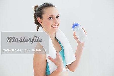 Portrait of a fit young woman with water bottle standing against the wall at fitness studio