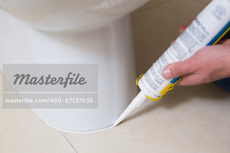 Close up of a plumber fixing toilet in a washroom with silicone cartridge