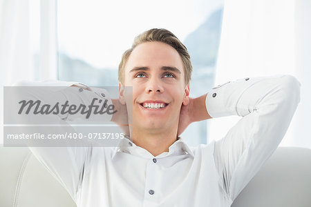 Close up of a smiling relaxed young man sitting on sofa in a bright house