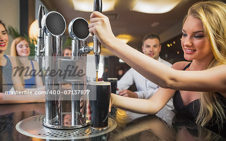 Attractive woman pulling a pint of stout in front of her friends in a restaurant