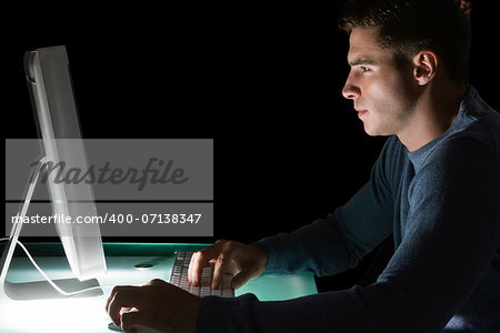 Handsome serious computer engineer looking at computer at night at his lit desk