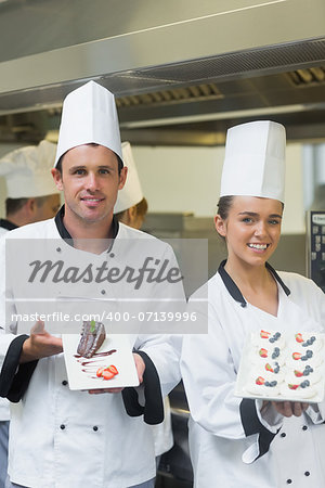 Two happy chefs presenting dessert plates smiling at the camera