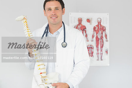 Handsome content doctor holding skeleton model in bright office