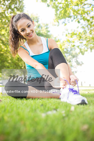 Cheerful active brunette tying her shoelaces in a park on a sunny day