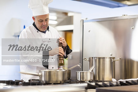 Focused head chef flavoring food with pepper in professional kitchen