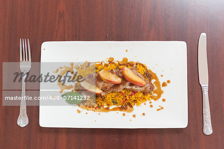Overhead view of couscous dish with meat and apple on white plate