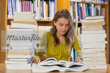 Concentrating pretty student studying between piles of books in library