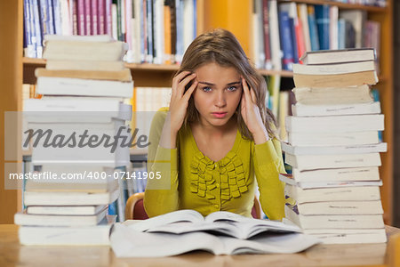 Tired pretty student studying between piles of books in library