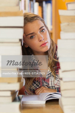 Unsmiling pretty student studying between piles of books in library