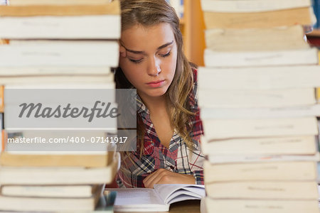 Concentrated pretty student studying between piles of books in library