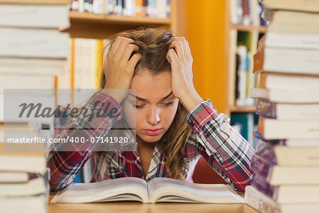 Irritated pretty student studying between piles of books in library