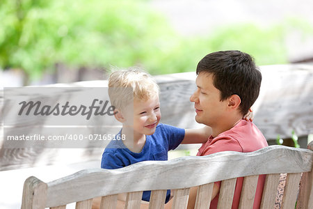 smiling positive father and his smiling adorable son sitting together and spending fun time outdoors