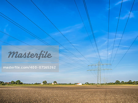 Power cable and power pole over a field under a blue sky with white clouds