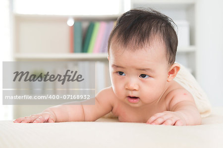 Adorable six months old Asian baby girl crawling on bed.