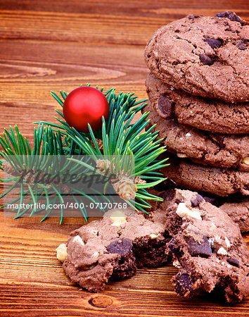 Stack of Delicious Christmas Chocolate Cookies with Green Spruce Branch and Red Bauble closeup on Wooden background