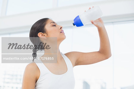 Fit young woman drinking water in fitness studio