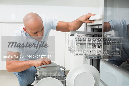 Serious young man using dish washer in the kitchen at home